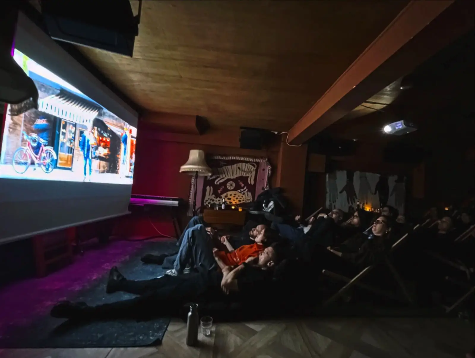 The basement set up for a screening, rows of low seats facing the projector