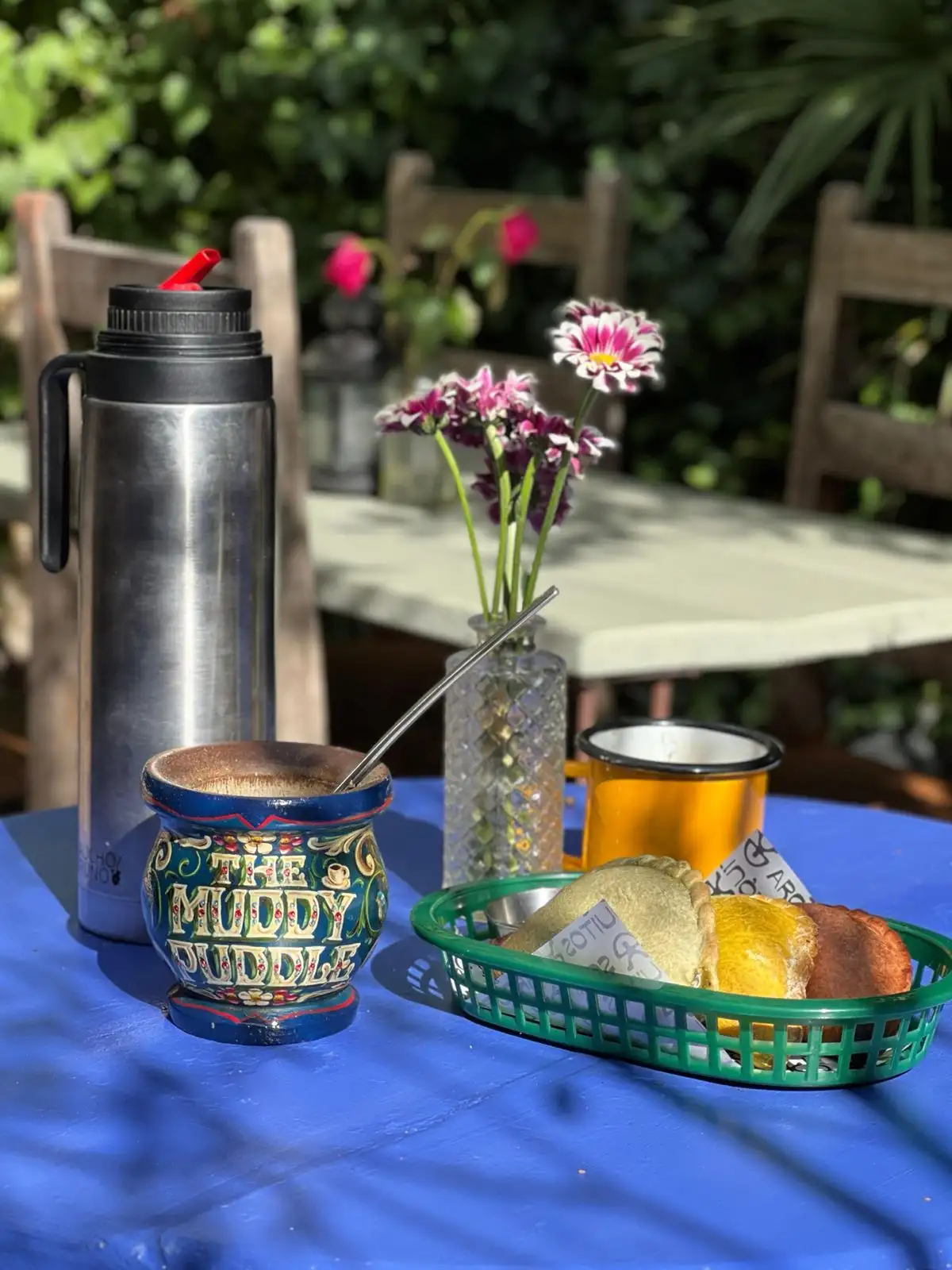 Mate, a flask, flowers and a basket of empanadas on a blue table in the garden