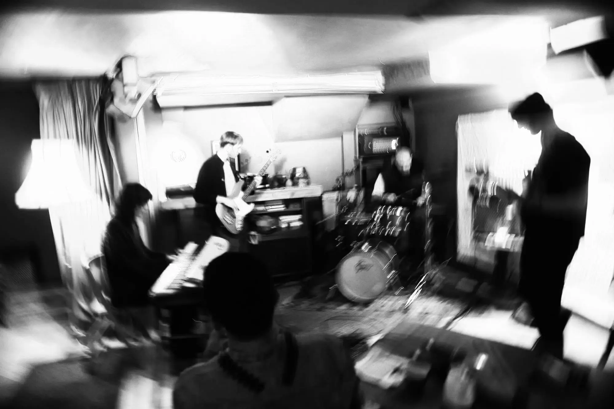 A band rehearsing in the basement on keys, bass and drums, in black and white